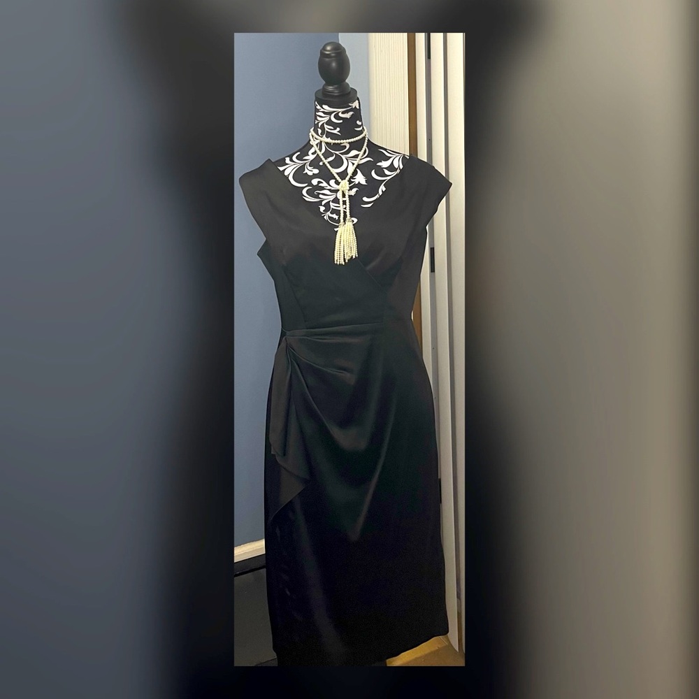 Black satin sleeveless sheath dress with front ruffle and criss cross bodice.